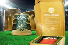 an open box containing two cans of beer on a green field with stadium lights in the background