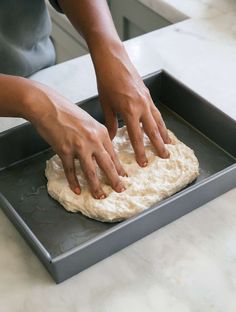 a person kneading dough on top of a black baking sheet in a kitchen