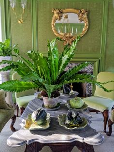 a dining room table with green chairs and potted plants on it in front of a fireplace