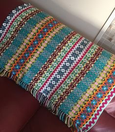 a multicolored blanket sitting on top of a brown couch next to a pillow