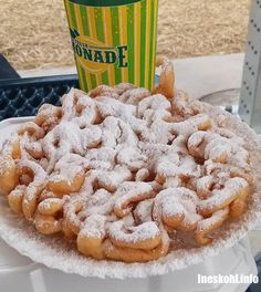 powdered sugar covered donuts sitting on top of a white plate next to a cup