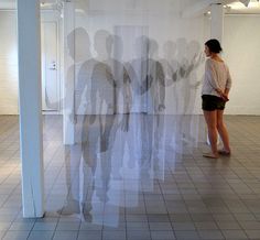 a woman is standing in an empty room with white walls and tile flooring, looking at artwork on the wall