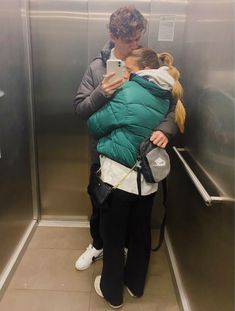 a woman holding a child in her arms while standing next to an elevator