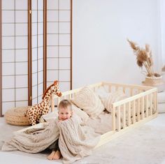 a little boy that is sitting on the ground in front of a bed with a giraffe