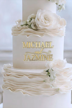 a white wedding cake with gold lettering and flowers