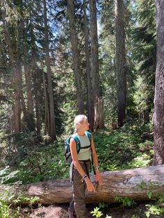 a woman with a backpack standing next to a large log in the middle of a forest