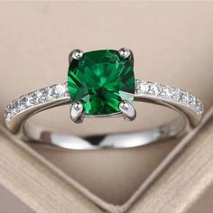 a ring with a green stone surrounded by white diamonds in a box on top of a table