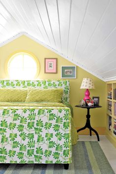 a green and white bed sitting under a window next to a table with a lamp