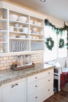 the kitchen is decorated for christmas with wreaths on the shelves and dishes in the cabinets