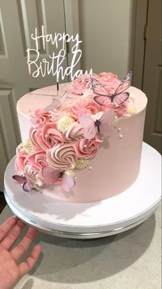 a birthday cake with pink flowers and butterflies on top is being held up by someone's hand