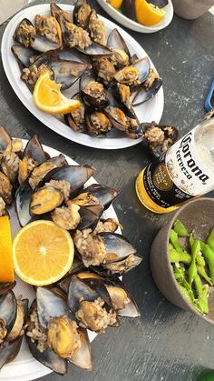 two plates filled with mussels and orange slices on a table next to bottles of beer