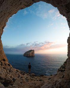 a person standing in the middle of a cave looking out at the ocean and rock formations