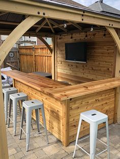 an outdoor bar with stools and a television on the back wall in front of it