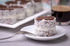 a piece of cake on a plate with a fork next to it and a cup of coffee in the background