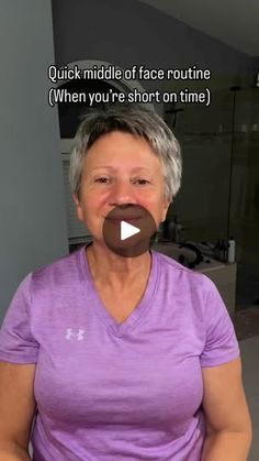 an older woman with grey hair and purple shirt holding a chocolate donut in front of her face