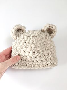 a hand is holding up a crocheted bear head purse on a white background