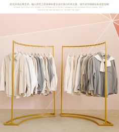 two racks with clothes hanging on them in front of a pink wall