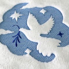 two white doves flying in the night sky with stars on their wings, embroidered onto a blue and white towel