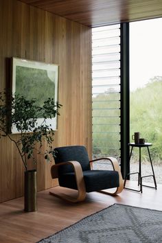 a black chair sitting in front of a wooden wall next to a tall vase filled with plants