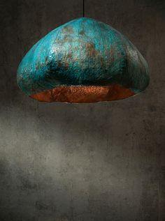 a green and copper colored light hanging from a ceiling fixture in a room with concrete walls