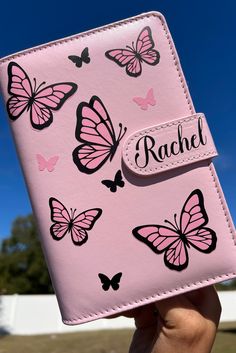 a pink wallet with butterflies on it and the name rachel written in black ink is held up by a person's hand