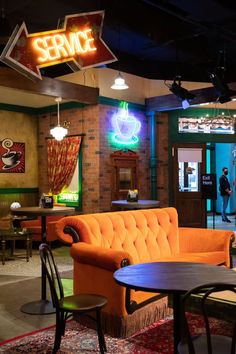 an orange couch sitting in the middle of a room with tables and chairs around it