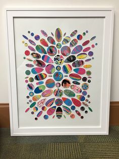 a white framed art print with colorful circles and words on the bottom, in front of a carpeted wall