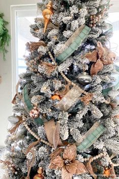 a decorated christmas tree in front of a window with gold and silver ornaments on it