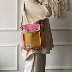 a woman is holding a pink and yellow handbag in front of a white wall