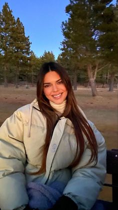 a woman sitting on top of a bench in front of some trees and smiling at the camera