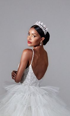 a woman in a white dress with a tiara on her head and hands behind her back