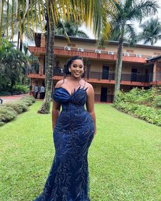 a woman standing in front of a palm tree wearing a blue dress with an off the shoulder neckline