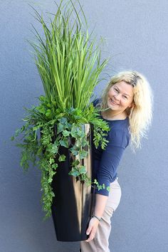 a woman standing next to a tall planter with green plants on it's sides