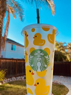 someone holding up a starbucks cup with rubber ducks on it and palm trees in the background