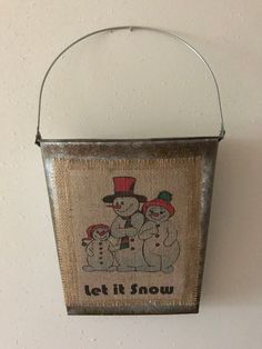 a metal bucket hanging on the wall with a snowman and two dogs in it