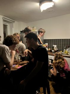 a group of people sitting at a table in a kitchen with food on the counter