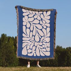 a blue and white blanket hanging from the side of a field with trees in the background