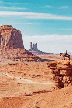 a man riding a horse on top of a cliff in the middle of desert land