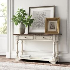 a white table with two vases on it and a framed flower arrangement next to it