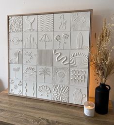 a vase sitting on top of a wooden table next to a white wall with many different designs