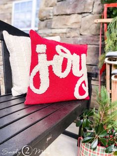 a red and white pillow sitting on top of a wooden bench next to potted plants