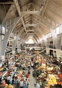 an indoor market filled with lots of food and people walking through the aisles, surrounded by tall ceilings