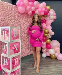 a pregnant woman standing in front of pink and gold balloons