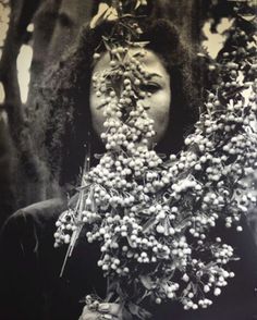 a black and white photo of a woman's face surrounded by berries on a tree