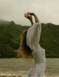 a woman in a white dress reaching up into the air