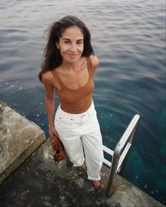 a woman standing on the edge of a pier next to water and holding a purse