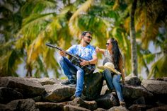 a man and woman sitting on rocks with palm trees in the backgroung