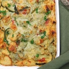 a square casserole dish filled with vegetables and cheese on a green table cloth