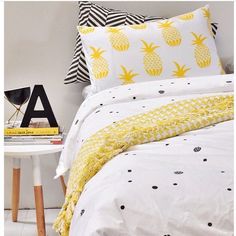 a bed with yellow pineapples on it next to a white table and chair