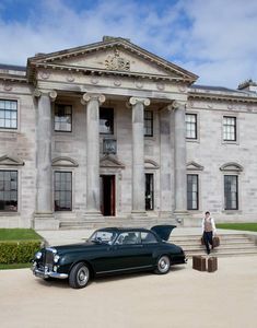 an old black car parked in front of a large building with columns on the side